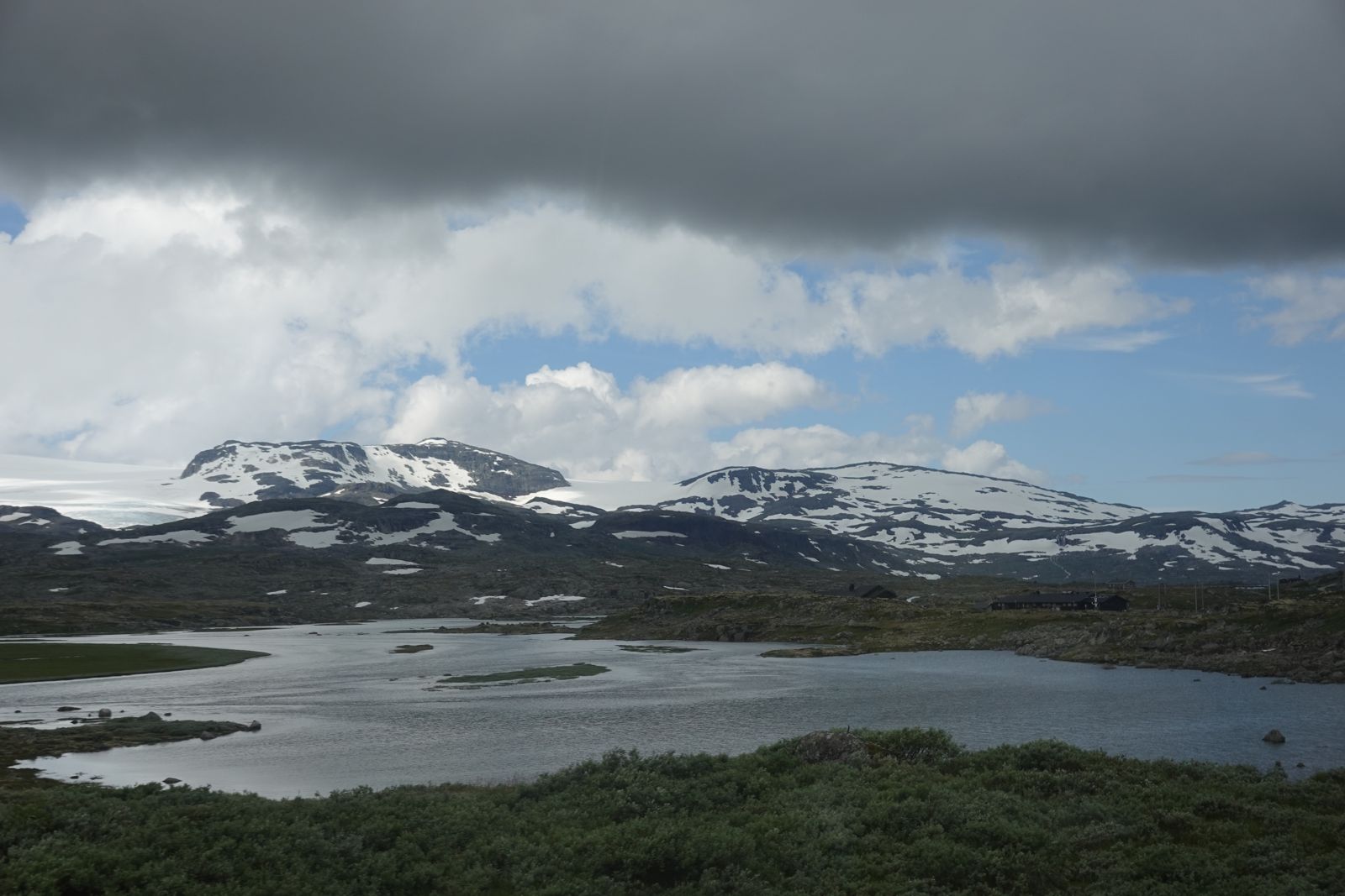 Snow-dusted mountains above a highland lake under dark clouds
